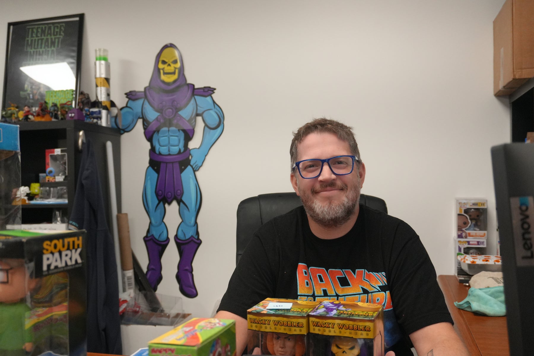 Adam, Channel Manager at Jay’s Toys & Games, at his desk in front of a Skeletor wall cut-out